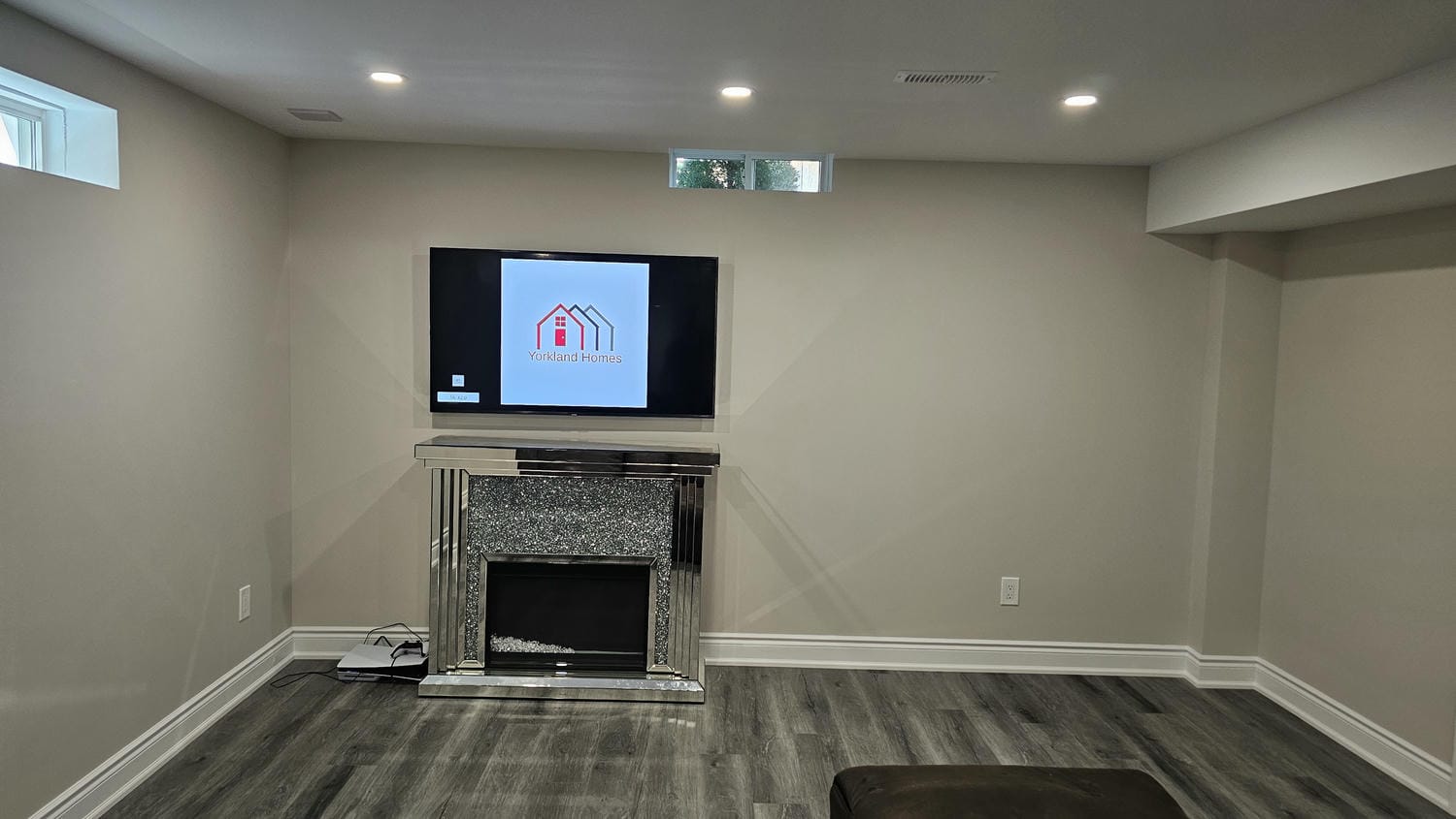 basement living room wall with fireplace and TV that has Yorkland Homes Logo on the tv screen