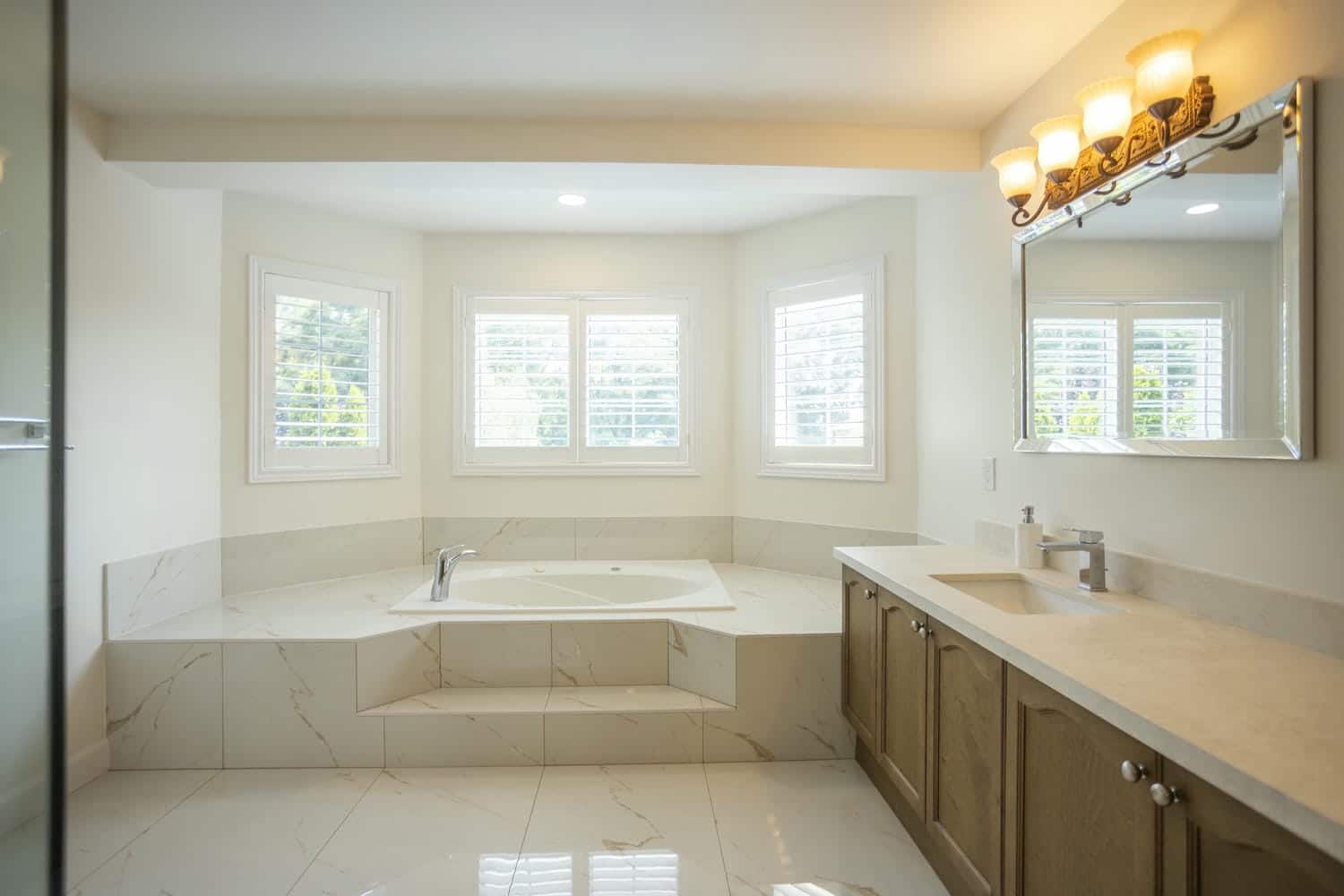 Large mirror with a 4 bulb light fixture above a quartz countertop