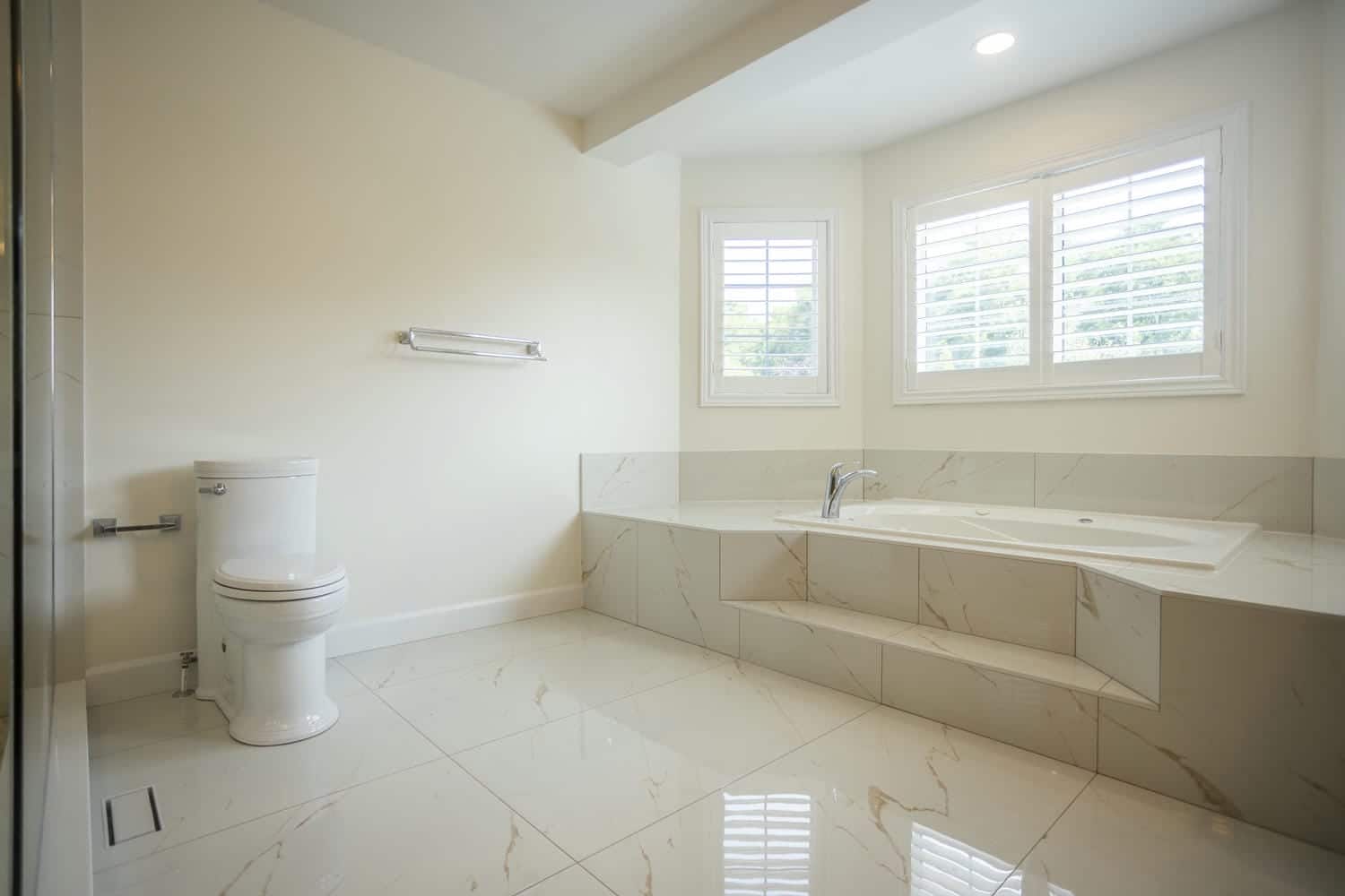 Chrome towel rack and toilet paper holder with a large spacious area between the bathtub and the toilet