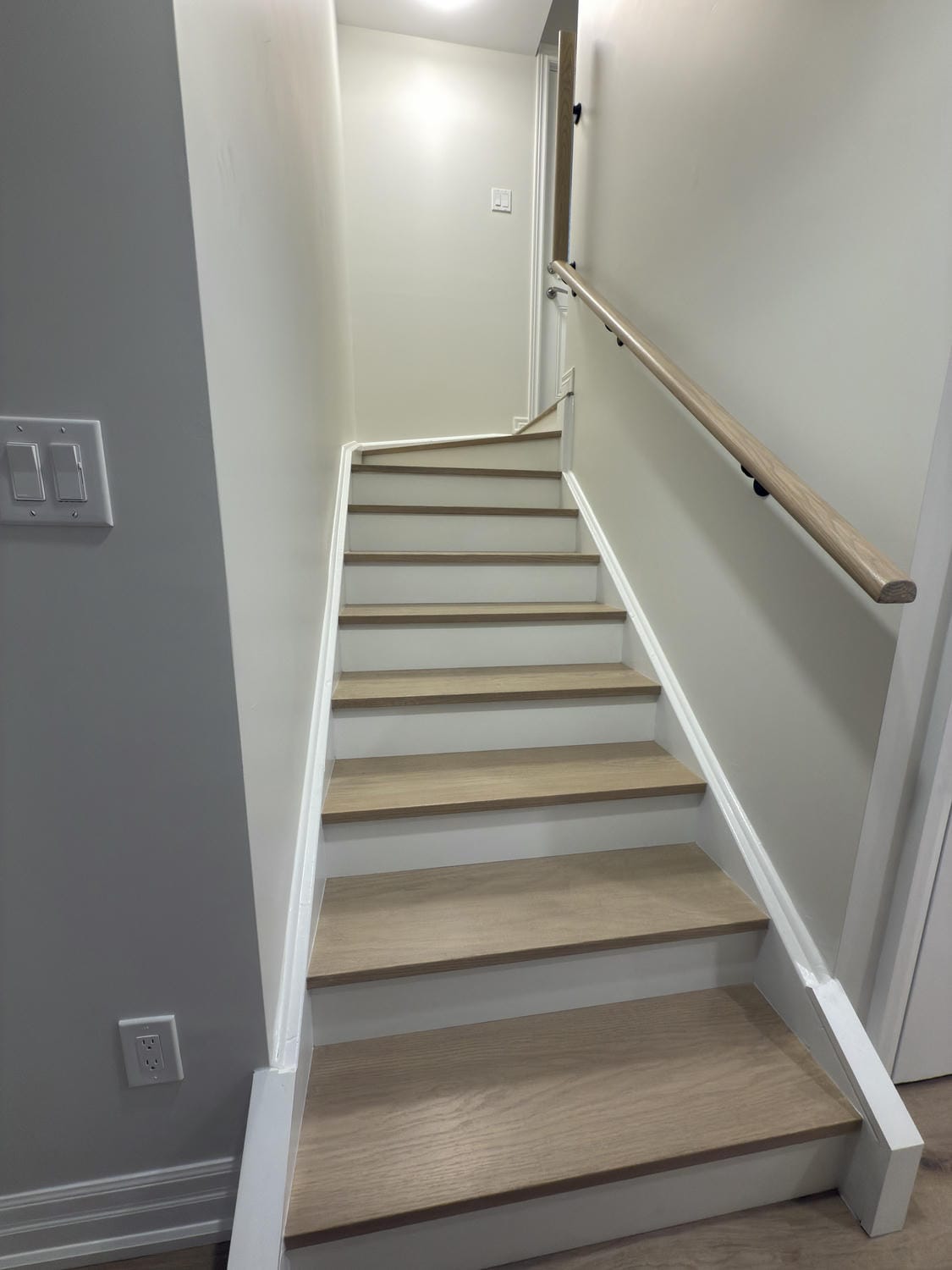 Clean oak stair treads with crisp white risers for a bright, modern entry. Simple railing detail keeps the space sleek and functional.