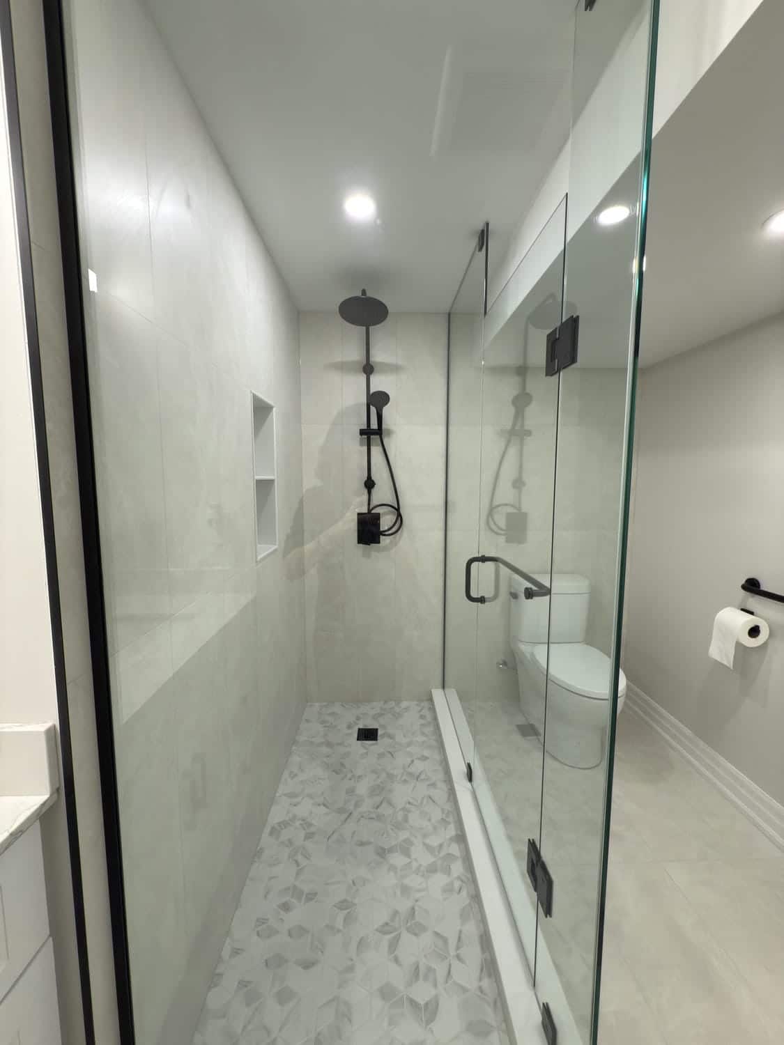 Spacious walk-in shower with full glass enclosure and clean tile work. Matte black fixtures and a built-in niche add a modern edge