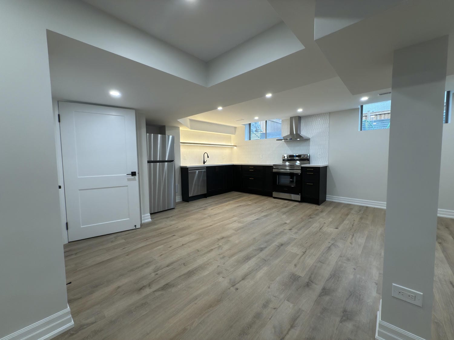 Open basement layout with a sleek kitchenette and plenty of space to relax. Warm flooring and recessed lighting create a bright, inviting feel.